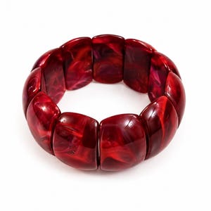 Op de afbeelding: Een opvallende rode armband met een marmer effect. De armband bestaat uit rechthoekige, afgeronde segmenten, waardoor een opvallend accessoire ontstaat. De kleur is een diep, rijk rood met wervelende patronen.