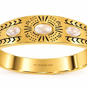 Peut inclure: Un bracelet jonc articulé en acier inoxydable doré orné de trois pierres cabochons ovales blanches. La surface présente des motifs géométriques noirs gravés et des rayons de soleil. L'intérieur porte l'inscription WL Stainless steel.
