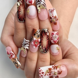May include: A set of long, decorated fingernails. Designs include floral patterns, zebra stripes, and abstract radial patterns in shades of red, brown, and white. Some nails feature gold embellishments and a pink base.