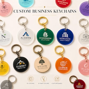 May include: A collection of round acrylic keychains in various colors, each featuring a unique business logo and name. The keychains are attached to metal rings in gold, silver, bronze, or rose gold tones. The text CUSTOM BUSINESS KEYCHAINS is visible.
