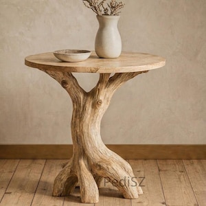 Könnte beinhalten: Ein runder Beistelltisch aus Holz mit einem natürlichen Baumstammfuß. Auf der Tischplatte befinden sich eine kleine Keramikschale und eine cremefarbene Vase mit getrockneten Zweigen. Der Tisch steht auf einem Holzboden.