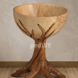 May include: A wooden bowl with a tree trunk base. The bowl is light-coloured, with a darker, textured base resembling tree roots. The word "pedisy" is visible on the front of the bowl. The bowl is displayed on a wooden floor.