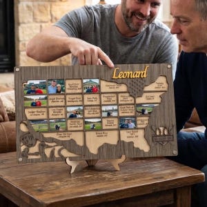 May include: A rectangular wooden display board shaped like a map of the United States, featuring the name Leonard in script, slots for small photographs, and engraved baseball-themed graphics including a glove, bat, and ball on the left side.