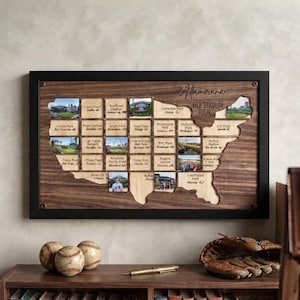 May include: A rectangular wooden wall display featuring a map of the United States with cutouts for photos and text labels of MLB stadiums. The piece is framed in black and includes the engraved text Altamirana MLB STADIUM TOUR.