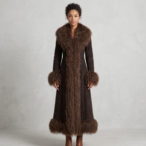 May include: A full-length brown coat with a faux fur collar, cuffs, and trim. The coat has a suede-like texture and a tailored fit. The faux fur is a darker shade of brown, creating a contrast. The coat is a statement piece.