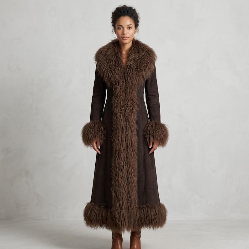 May include: A full-length brown coat with a faux fur collar, cuffs, and trim. The coat has a suede-like texture and a tailored fit. The faux fur is a darker shade of brown, creating a contrast. The coat is a statement piece.