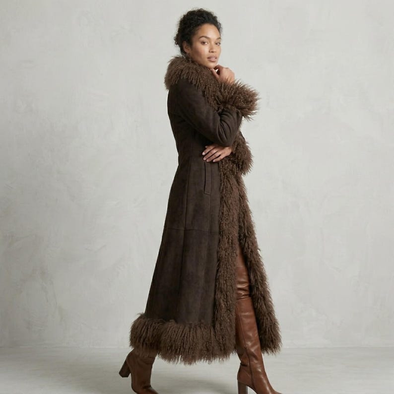 May include: A long, dark brown coat with a faux fur trim around the collar, cuffs, and hem. The coat is made of a suede-like material and has a tailored fit. The model is wearing brown leather boots.