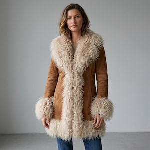 May include: A brown suede coat with a cream-colored, shaggy trim around the collar, cuffs, and front opening. The coat has a mid-length cut and a warm, textured appearance, suitable for cold weather.