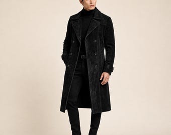 May include: A black suede double-breasted trench coat with wide lapels, long sleeves, and a button-front closure. The coat is worn over a black turtleneck sweater and black trousers, paired with black leather boots, creating a monochromatic look.