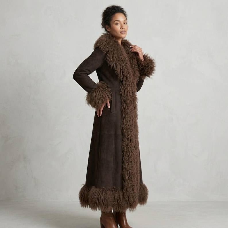 May include: A long, dark brown coat with a faux fur trim around the collar, cuffs, and hem. The coat is made of a suede-like material and has a tailored fit. The model is wearing brown boots.