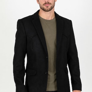 Könnte beinhalten: Ein schwarzer Blazer mit einem Western-Style-Joch auf der Brust, einem steigenden Revers und zwei Knöpfen auf der Vorderseite. Das Kleidungsstück wird über einem schlichten olivgrünen T-Shirt getragen. Der Blazer hat zwei Pattentaschen an der Taille.