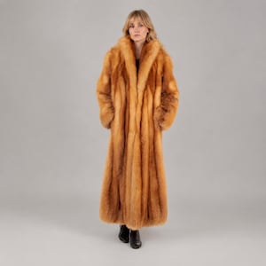 May include: A full-length, long-sleeved coat made of thick, textured fur in shades of golden-brown, orange, and cream. The coat features a wide, prominent collar that extends down the front, creating a voluminous silhouette with a straight hemline.