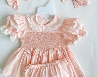 Gesmokte jurk babymeisjes met bloemen en strik. Traditionele Spaanse stijl, perzik