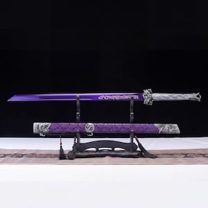 Könnte beinhalten: Ein violettes Schwert mit einem silbernen Griff mit aufwendigen Metallarbeiten und einer passenden violetten Scheide, die mit silbernen Akzenten und einem Yin-Yang-Symbol verziert ist. Das Schwert ruht auf einem schwarzen Ständer mit schwarzen Quasten.