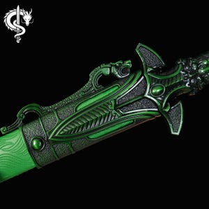 Pu&ograve; includere: Primo piano di una spada decorativa verde con intricati dettagli a tema drago. La spada presenta un'impugnatura e una guardia della lama strutturate, con un design a testa di drago sull'elsa. La lama ha un motivo strutturato.