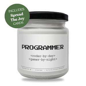 Może przedstawiać: Biała świeca w przezroczystym szklanym słoiku z czarną pokrywką. Etykieta zawiera tekst PROGRAMMER, <coder-by-day> oraz <gamer-by-night>. Zielona okrągła plakietka w lewym górnym rogu wyświetla tekst INCLUDES Spread The Joy CARDS.