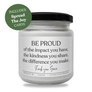 Op de afbeelding: Een kaars in een doorzichtige glazen pot met een zwarte deksel en witte was. Het etiket bevat de tekst: BE PROUD of the impact you have, the kindness you share, the difference you make. Thank you, Grace. Een groene ronde badge vermeldt: INCLUDES Spread The Joy CARDS.