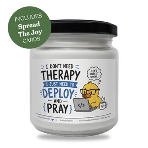 Pode incluir: Uma vela de cera de soja branca num frasco de vidro transparente com tampa preta. O rótulo apresenta um pato amarelo de óculos a usar um portátil com o texto: I DON'T NEED THERAPY I JUST NEED TO DEPLOY AND PRAY, LET'S HOPE IT WORKS. Inclui cartões Spread The Joy.