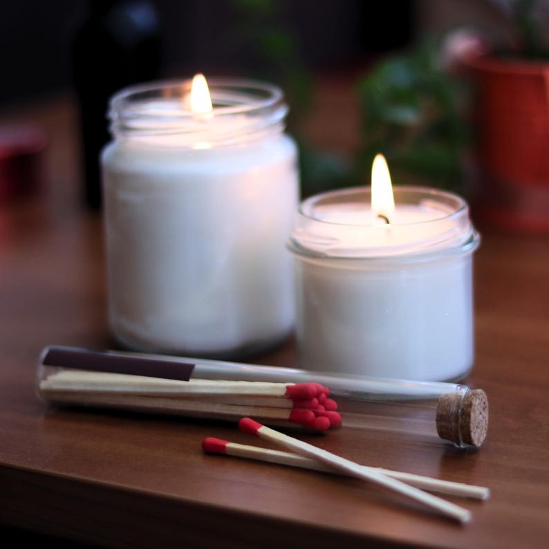 two lit candles in glass jars, along with a collection of red matchsticks, all placed on a wooden surface.