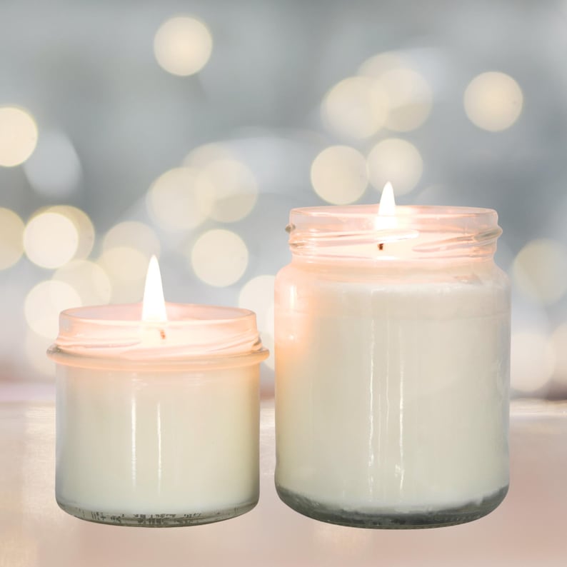 Peut inclure: Deux bougies allum&eacute;es dans des bocaux en verre transparent de hauteurs diff&eacute;rentes. Chaque bougie pr&eacute;sente une cire blanche et une m&egrave;che allum&eacute;e centr&eacute;e au sommet. Les bocaux en verre ont une forme cylindrique simple avec un rebord visible.