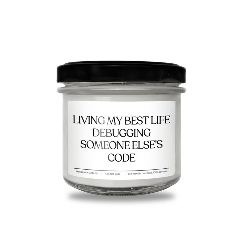 Peut inclure: Une bougie en pot de verre transparent avec un couvercle noir et une &eacute;tiquette blanche portant le texte noir : LIVING MY BEST LIFE DEBUGGING SOMEONE ELSE'S CODE. L'&eacute;tiquette inclut aussi : Handmade with heart | Candele Belle | Eco-friendly, non-toxic, 100% soy wax.