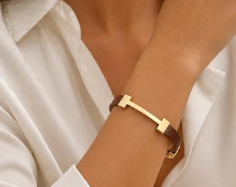 Bracciale in pelle marrone con barretta dorata, minimalista, elegante, con cinturino.