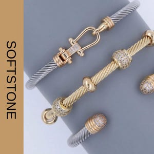 May include: Three bracelets with silver and gold tones. One bracelet has a gold clasp with clear stones. Another has gold accents and clear stones. The third bracelet has gold accents with clear stones. The text "SOFTSTONE JEWELRY" is on the left.