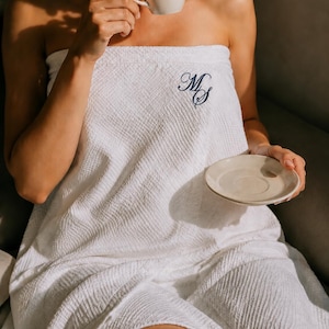 May include: A white waffle-weave bath wrap featuring a dark blue embroidered monogram with the letters MS. The fabric has a textured, grid-like pattern throughout, and the wrap is secured around the upper body with a straight, clean edge.