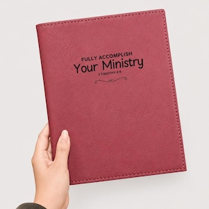 Könnte beinhalten: Ein kastanienbraunes Notizbuch mit texturierter Oberfläche, das den schwarzen Aufdruck "FULLY ACCOMPLISH Your Ministry 2 TIMOTHY 4:5" mittig auf der Vorderseite sowie ein kleines dekoratives Schnörkel-Element unter der Bibelstelle zeigt.