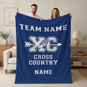 May include: A dark blue fleece blanket featuring white text that reads TEAM NAME, CROSS COUNTRY, and NAME. In the center, a large white graphic displays the letters XC with a winged arrow design running horizontally through the middle.