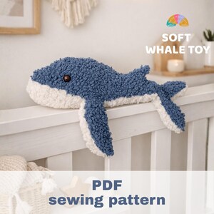 Peut inclure: Une peluche baleine en tissu texturé bleu et blanc avec un œil marron foncé. Le jouet présente une tête arrondie, des nageoires latérales et une queue. Le texte sur l'image indique SOFT WHALE TOY et PDF sewing pattern en lettres bleues et blanches.