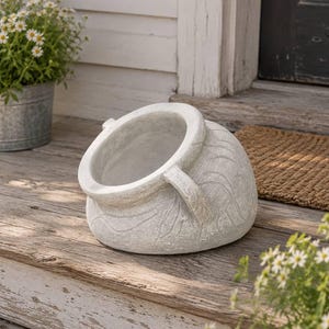 May include: A light gray, weathered-look ceramic planter pot with a wide, angled opening and two side handles. The exterior surface features a subtle, carved swirling pattern, giving it a textured appearance. The pot is positioned on its side.