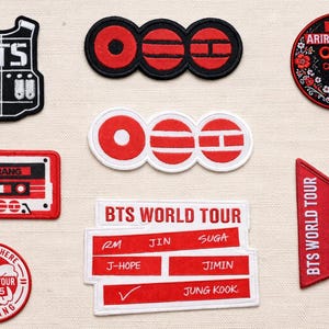 May include: A collection of embroidered patches in red, black, and white. Designs include the text "BTS", a cassette tape, and the words "BTS WORLD TOUR" with member names. Other patches feature floral and geometric designs.