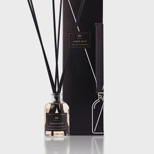 May include: An aromatherapy diffuser with black reeds and a black box. The glass bottle contains a light amber liquid. The label reads "-89- aromatic AMBER DUST". The box has a minimalist design with the same label and a bottle outline.
