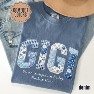May include: A denim blue t-shirt with the name "GIGI" appliqued in patchwork fabric. The letters are in various shades of blue and white with floral and gingham patterns. Below the name are the names Oliver, Sophie, Noah, Bailey, and Mia.