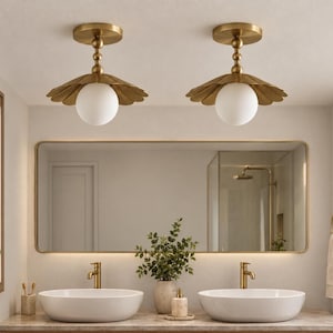 May include: Two ceiling-mounted light fixtures featuring a brushed brass finish, a tiered stem, a scalloped metal shade, and a central spherical white glass globe. These fixtures provide downward illumination and are mounted to a flat ceiling surface.
