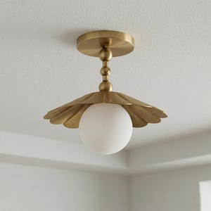May include: A brass-coloured ceiling light fixture with a scalloped shade and a white globe light. The fixture is mounted on a white ceiling. The shade has a petal-like design.