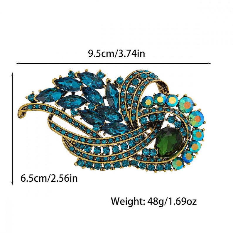 K&ouml;nnte beinhalten: Verzierte Brosche mit goldfarbener Metallbasis, verziert mit t&uuml;rkisblauen und irisierenden Kristallen. Die Brosche ist 9,5 cm lang und 6,5 cm breit und wiegt 48 g. Sie hat einen gro&szlig;en gr&uuml;nen Mittelstein.