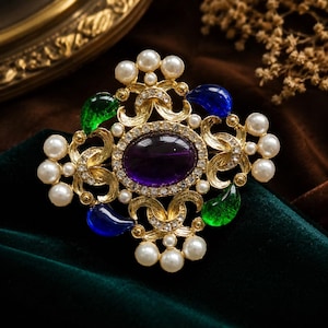 May include: A gold-toned brooch with an oval purple center stone surrounded by clear crystals. The brooch features pearl accents, green and blue teardrop-shaped stones, and ornate gold filigree details. A luxurious and elegant accessory.