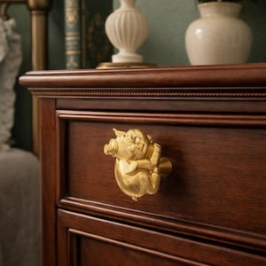 May include: A close-up of a dark brown wooden dresser drawer with a gold-colored pig-shaped knob. The knob is detailed with the pig's features. The dresser is in a bedroom setting, with a lamp and vase visible in the background.