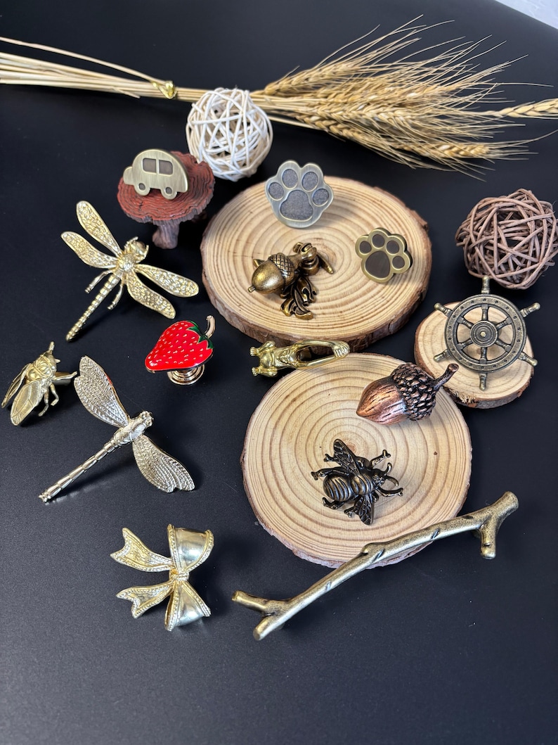 Puede incluir: Una colecci&oacute;n de tiradores y pomos decorativos para armarios en varias formas y colores. Incluye un coche, una lib&eacute;lula, un lazo, una abeja, una bellota, una huella de pata y un tim&oacute;n. Los pomos son de metal y madera.