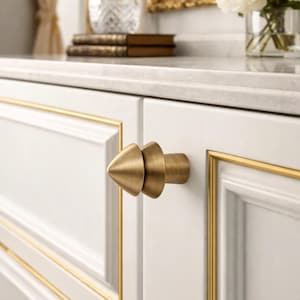 Könnte beinhalten: Nahaufnahme einer weißen Schranktür mit goldfarbenem Rahmen und einem konisch geformten Knopf in Messingoptik. Der Schrank ist Teil eines größeren Möbelstücks, möglicherweise einer Kommode oder einem Waschtisch. Das Design ist klassisch und elegant.