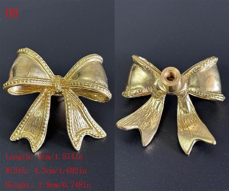 Puede incluir: Dos piezas de herrajes decorativos dorados en forma de lazo. Los herrajes miden 4 cm de largo, 4,3 cm de ancho y 1,9 cm de alto. Los herrajes tienen un orificio roscado en la parte posterior. El texto de la imagen dice: Longitud: 4 cm, Ancho: 4,3 cm, Altura: 1,9 cm.