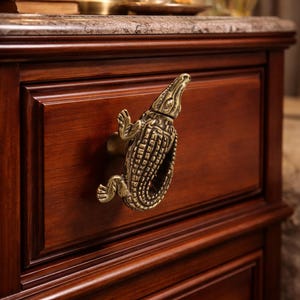 May include: A detailed close-up of a wooden drawer with a brass alligator-shaped handle. The drawer is part of a dark brown wooden cabinet. The alligator handle is intricately designed with textured scales and a detailed head.