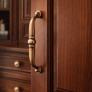 Puede incluir: Primer plano de una puerta de madera con un tirador de latón. La puerta es de un color marrón oscuro intenso, y el tirador tiene un diseño arqueado con detalles decorativos. El tirador está montado en la superficie de la puerta.