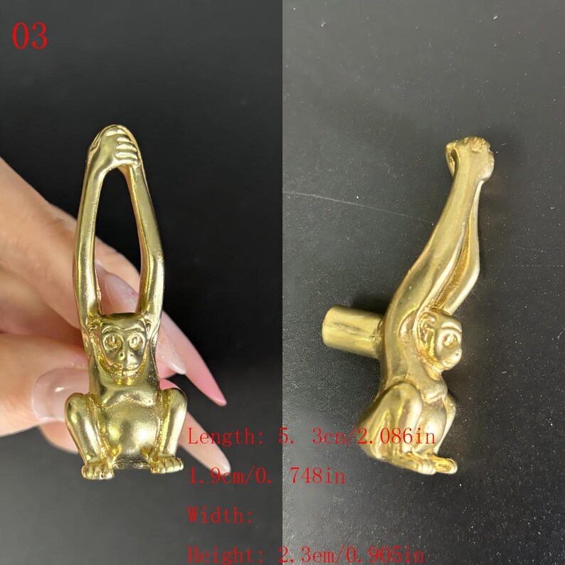 Puede incluir: Un tirador de armario con forma de mono de lat&oacute;n. El mono est&aacute; sentado con los brazos levantados. El tirador mide 5,3 cm de largo, 1,9 cm de ancho y 2,3 cm de alto. El n&uacute;mero "03" est&aacute; en la esquina superior izquierda.