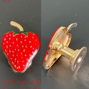 Puede incluir: Un broche decorativo con forma de fresa con acabado esmaltado rojo y detalles dorados. El broche mide 3 cm de ancho y 4 cm de alto. El dise&ntilde;o incluye hojas verdes y peque&ntilde;os puntos blancos.