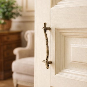 Peut inclure: Une poignée de porte en bronze en forme de branche d'arbre est fixée sur une porte à panneaux blanche. La poignée a un aspect naturel et rustique, ajoutant une touche de décoration inspirée de la nature à l'intérieur.