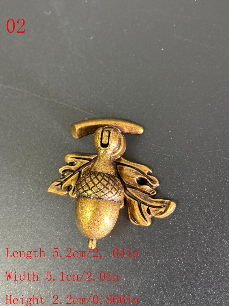 Puede incluir: Elemento decorativo en forma de bellota de color bronce. La bellota mide 5,2 cm de largo, 5,1 cm de ancho y 2,2 cm de alto. El dise&ntilde;o incluye hojas de roble y el n&uacute;mero "02" en la esquina superior izquierda.