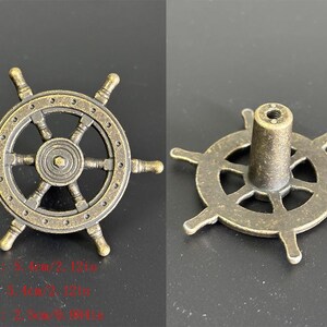 Puede incluir: Tirador de armario de color lat&oacute;n antiguo con forma de tim&oacute;n de barco. El tirador tiene un cubo central con radios y un borde circular con seis manijas. Dimensiones: Largo 5,4 cm, Ancho 5,4 cm, Alto 2,5 cm.